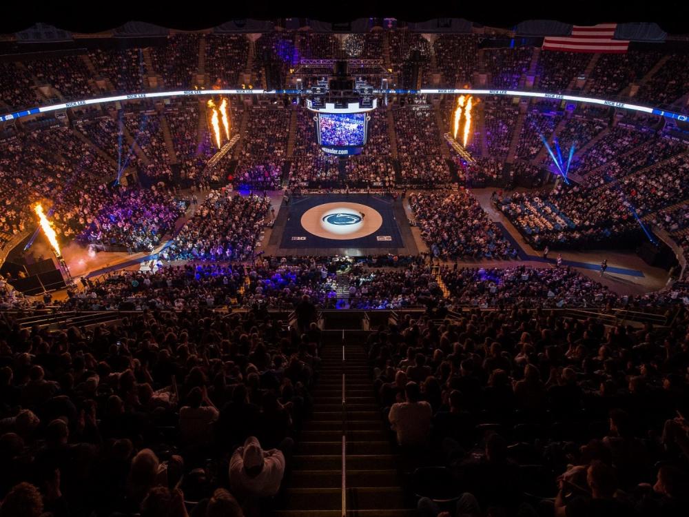 The interior of the Bryce Jordan Center with a packed crowd looking on at a wrestling mat in the center of the arena